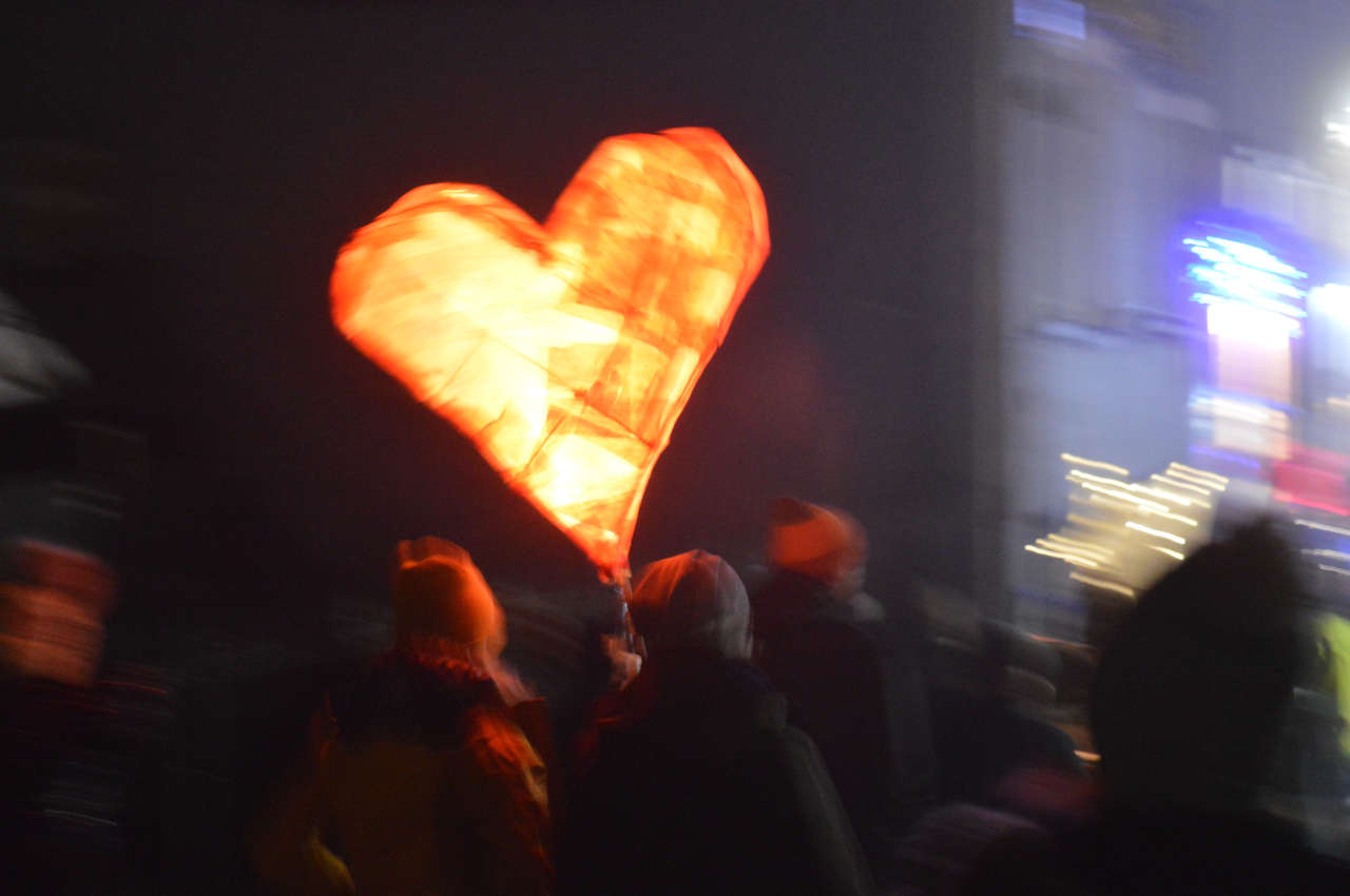 A heart shaped lantern being held up in a crowded street at night.